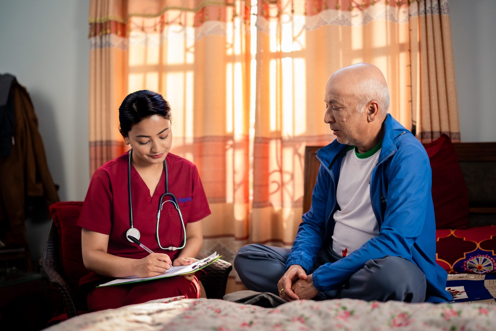 Nurse writing visit notes with an elderly man during a home visit in Kathmandu